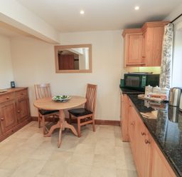 A kitchen with a round wooden table and two chairs a wooden cabinet microwave toaster and kettle on black countertop at Granary Cottage Blackwell near Ilmington