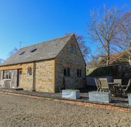 A stone cottage with wooden door and windows and outdoor seating area at Granary Cottage Blackwell near Ilmington