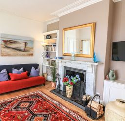 A living room with a red sofa pillows a fireplace with a gold framed mirror a red patterned rug and a wall mounted tv at Victoria Lodge in Kingsbridge