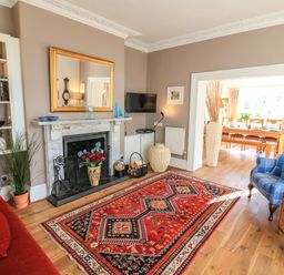 A living room with a fireplace a red patterned rug a blue armchair and a doorway to a dining area at Victoria Lodge in Kingsbridge