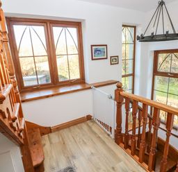 A staircase landing with wooden banisters and window frames and multiple windows showing an outdoor view at Nant Moel Isaf Farm in Rhydyfro near Pontardawe