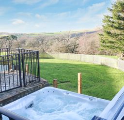An outdoor hot tub with bubbling water overlooking a fenced grassy yard and trees at Nant Moel Isaf Farm in Rhydyfro near Pontardawe
