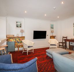 A living room with chairs a wall mounted television a red rug and a wooden table at Melvill Lower Deck in Falmouth