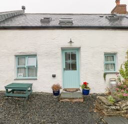 Exterior of a white cottage with a light blue door and windows surrounded by gravel and potted plants at Y Beudy in Crosswell Eglwyswrw near Newport Pembrokeshire
