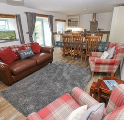 A living area with a brown leather sofa, plaid armchairs, a wooden dining table with chairs, and a kitchen in the background at Y Beudy in Crosswell Eglwyswrw near Newport Pembrokeshire