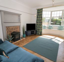 A living room with a fireplace a television and a bay window with cushions at Monarfon in Amlwch