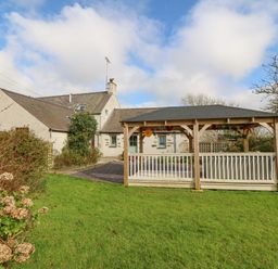 A garden with a wooden gazebo and a stone house in the background at Ty Gwennol in Llanfaethlu