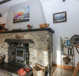 A living room with a stone fireplace and wooden stove at Ty Gwennol in Llanfaethlu