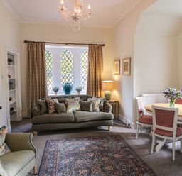 A living room with a sofa and armchair with cushions and a dining table with flowers at East Lodge - Crathes Castle in Crathes Castle near Banchory