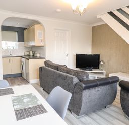A living room with grey sofas a television and a dining table next to a kitchen at 91 Waterside Park in Lowestoft