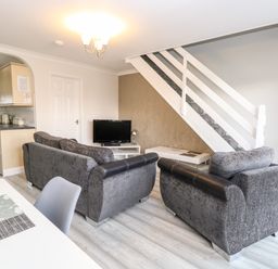 A living room with grey sofas a TV on a stand and a staircase next to an open kitchen at 91 Waterside Park in Lowestoft