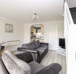 A living room with grey sofas a white dining table and chairs a TV on a stand and a staircase at 91 Waterside Park in Lowestoft