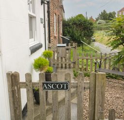 A wooden gate with a sign reading Ascot leading to a garden path with potted plants and a bench at Ascot Cottage in Sheriff Hutton near Strensall