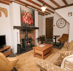A living room with a wood-burning stove paintings television and seating at Ascot Cottage in Sheriff Hutton near Strensall