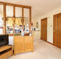 A living area with wooden furniture a television and a view into a kitchen at Hunters Lodge Great Moulton near Long Stratton