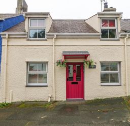 A small house with a red door and two windows on either side at Angorfa in Beaumaris