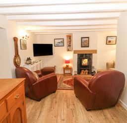 A living room with two leather armchairs a fireplace and a wall-mounted TV at Angorfa in Beaumaris