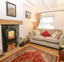 A living room with a wood stove fireplace a three seat sofa with cushions a floor lamp and a patterned rug at Angorfa in Beaumaris