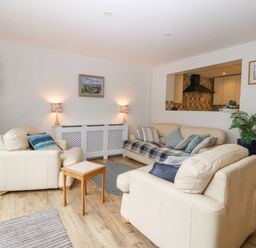A living room with beige leather sofas a small wooden table lamps and paintings at Angorfa in Beaumaris