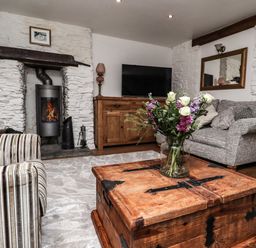 A living room with a stone fireplace wooden coffee table with flowers striped armchair and grey sofa at Garretts in Kingsand And Cawsand