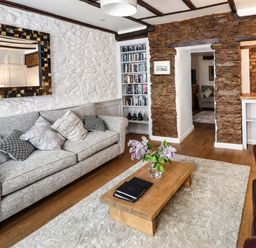 A living room with a grey sofa pillows wooden coffee table vase with flowers bookshelf stone wall and mirror at Garretts in Kingsand And Cawsand