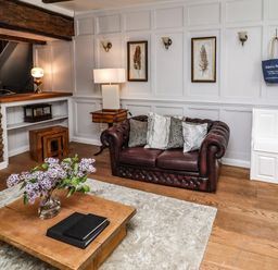 A living room with a brown leather sofa and pillows a wooden coffee table with a vase of flowers wooden floor and white paneled wall at Garretts in Kingsand And Cawsand