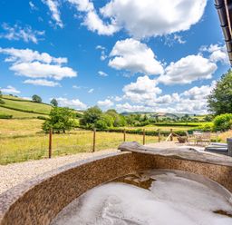 A hot tub overlooking a grass field and hills at Birch Banc Retreats - Bedw Llanidloes