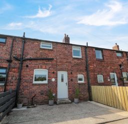 A brick terraced house with white door and windows and fenced front yards at The Miners Cottage in Scremerston near Berwick-Upon-Tweed