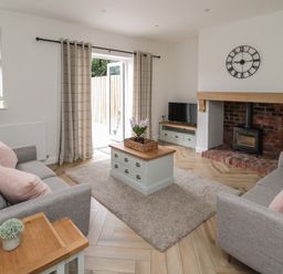A living room with two grey sofas pink cushions coffee table rug and fireplace at The Miners Cottage in Scremerston near Berwick-Upon-Tweed