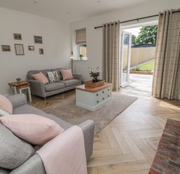 A living room with two sofas and a coffee table near open doors leading to a garden at The Miners Cottage in Scremerston near Berwick-Upon-Tweed