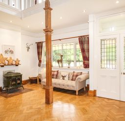A sitting area with a sofa and cushions next to a window with curtains and a wood stove in a room with wooden flooring at Deer Leap House in Moreton