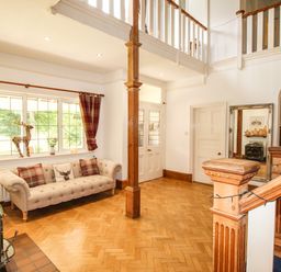 An entryway with a beige sofa under a window a wooden staircase and a large mirror at Deer Leap House in Moreton