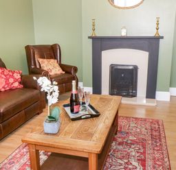 A living room with a brown sofa and armchair a wooden coffee table a fireplace and a red patterned rug at Hazeldene in Sleights