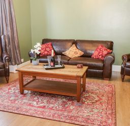 A living room with brown leather sofa and chairs red and beige cushions wooden coffee table with tray and bottle on a red patterned rug at Hazeldene in Sleights