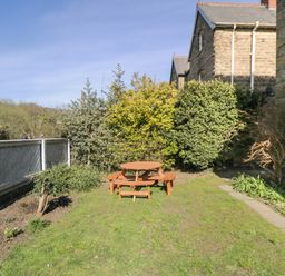 A garden with a wooden picnic table surrounded by shrubs and a stone house at Hazeldene in Sleights