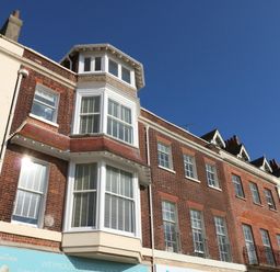 A row of red brick and white buildings with multiple windows under a clear blue sky at The Kings Statue in Weymouth