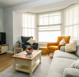 A living room with a gray sofa, orange and blue armchairs, wooden coffee table with fruit bowl and TV at The Kings Statue in Weymouth
