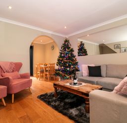 A living room with a Christmas tree and pink armchair near a wooden coffee table at The Seventeen in Bourton-On-The-Water