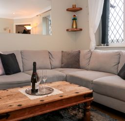 A living room with a grey sectional sofa and wooden coffee table with a bottle and glasses at The Seventeen in Bourton-On-The-Water