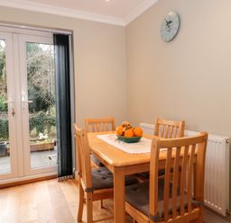 A dining area with a wooden table and four chairs and a bowl of fruit on the table near glass doors at The Seventeen in Bourton-On-The-Water