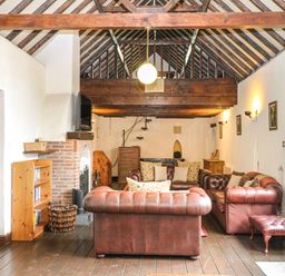 A living room with exposed wooden beams leather sofas a fireplace and a wooden floor at The Old Barn in Walcott