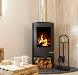 A room with a wood burning stove with firewood underneath and fireplace tools next to it at The Old Post Office in Porthleven