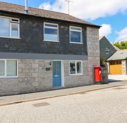 A stone house with blue door and red postbox on the street at The Old Post Office in Porthleven