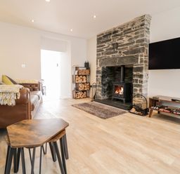 A living room with a leather sofa wood burning stove and a wall mounted television at Cooper's Rest Gorffwysfa Coopers in Dolwyddelan