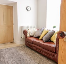 A room with a brown leather sofa with cushions and a wooden door at Cooper's Rest Gorffwysfa Coopers in Dolwyddelan