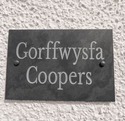 A black plaque with the text Gorffwysfa Coopers mounted on a white textured wall at Coopers Rest Gorffwysfa Coopers in Dolwyddelan