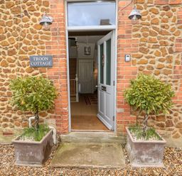 An open front door of a stone and brick cottage with two potted plants on either side at Troon Cottage Hunstanton
