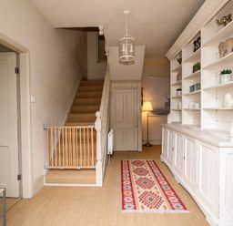 A hallway with a staircase and baby gate a white cabinet with shelves and a patterned rug at Troon Cottage in Hunstanton