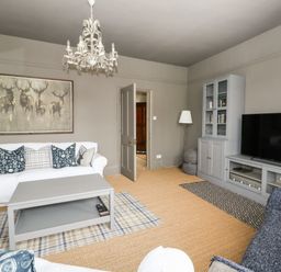 A living room with sofas cushions a coffee table a TV cabinet and a chandelier at Troon Cottage in Hunstanton