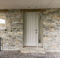 A stone exterior wall with a light gray door and adjacent window at Willow Barn in Shapwick